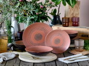 Schwarz-rosafarbenes Keramik-Geschirrset mit strukturierter Spiralglasur (großer und kleiner Teller sowie Schale) dekorativ auf Holztisch arrangiert, fotografiert in leicht schräger Frontansicht auf Tischhöhe.