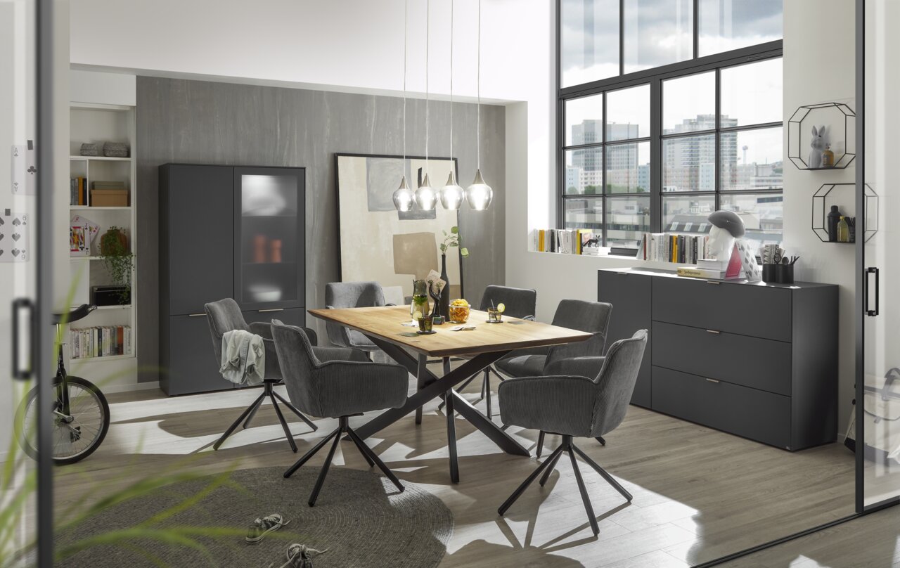 Set one by Musterring Esstisch SET ONE LAKEWOOD Moderner Esstisch mit Holzplatte und schwarzen Metallbeinen, umgeben von grauen Stühlen in einem stilvollen Esszimmer mit großen Fenstern und urbanem Ausblick, seitliche Perspektive.