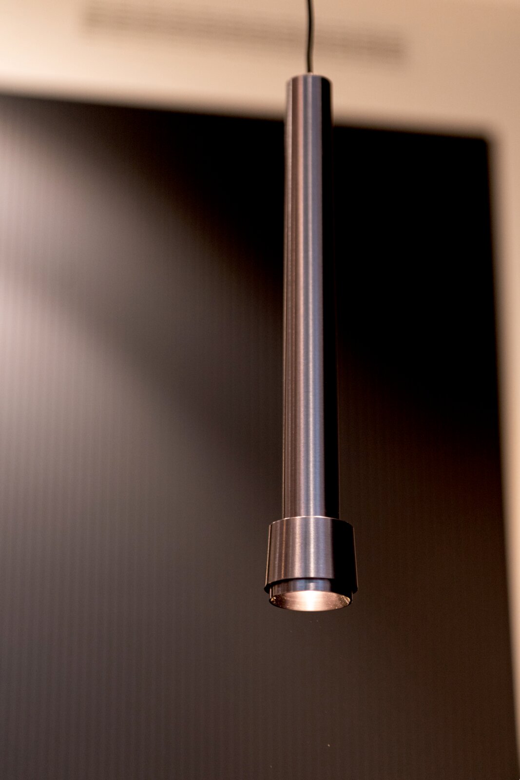 Lucide LED-Hängeleuchte für Stromschiene LINIAL Zylindrische Pendelleuchte aus gebürstetem Metall mit warmem Licht, Detailansicht aus leicht seitlicher Untersicht vor dunklem Hintergrund