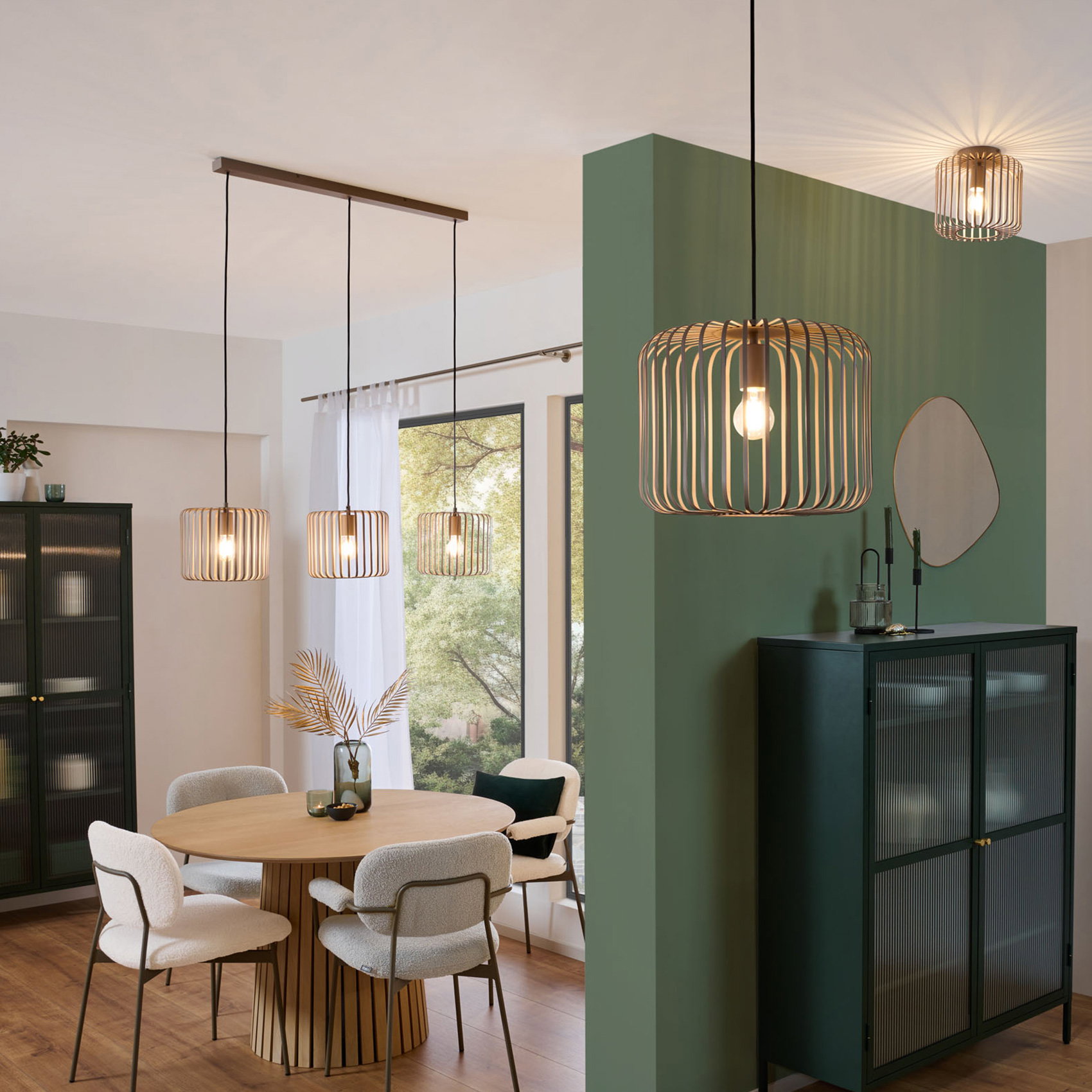 Moderne Esszimmerleuchten aus Holz über rundem Esstisch in hellem Wohnraum mit grüner Akzentwand.