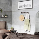 Moderne Wandgarderobe mit Haken, an der ein Strohhut und ein grüner Mantel hängen, in einem stilvoll eingerichteten Schlafzimmer mit Betonwänden. Perspektive von der Seite.