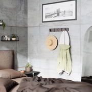 Moderne Wandgarderobe mit Haken, an der ein Strohhut und ein grüner Mantel hängen, in einem stilvoll eingerichteten Schlafzimmer mit Betonwänden. Perspektive von der Seite.
