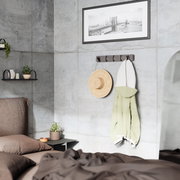 Moderne Wandgarderobe mit Haken, an der ein Strohhut und ein grüner Mantel hängen, in einem stilvoll eingerichteten Schlafzimmer mit Betonwänden. Perspektive von der Seite.