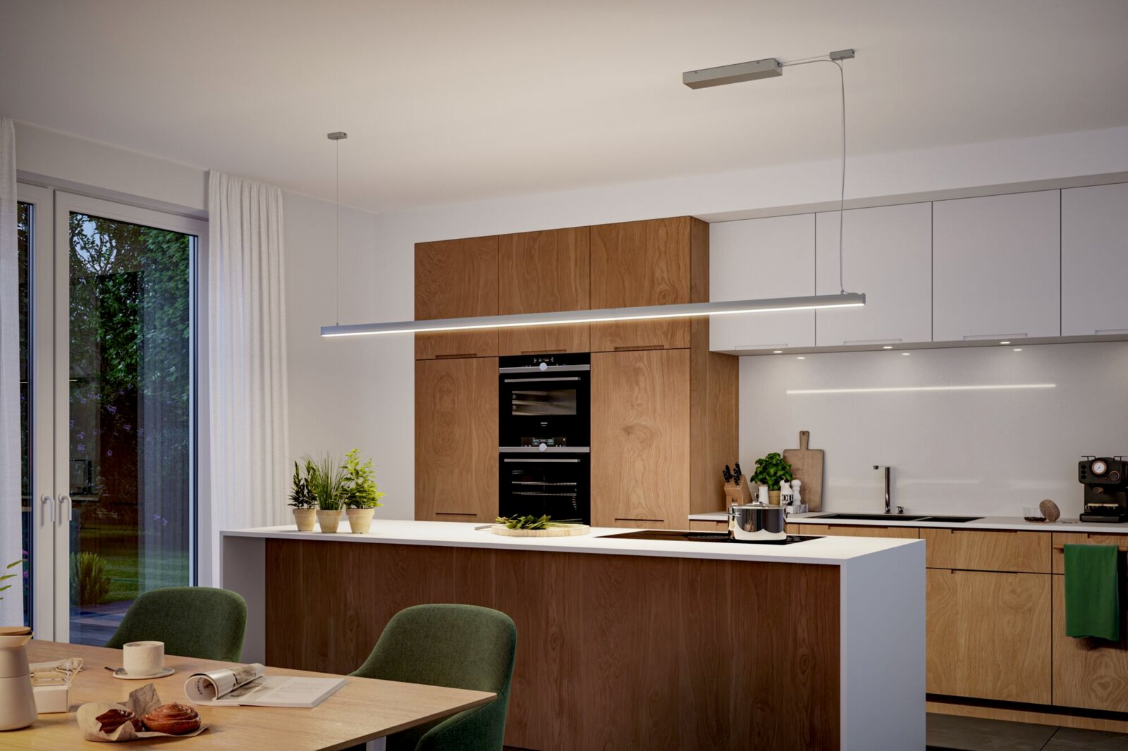 Moderne Küche mit Kücheninsel in Holz- und Weißoptik, integrierten Backöfen und langer LED-Pendelleuchte über der Arbeitsfläche, fotografiert in frontaler Innenraum-Perspektive auf Augenhöhe.