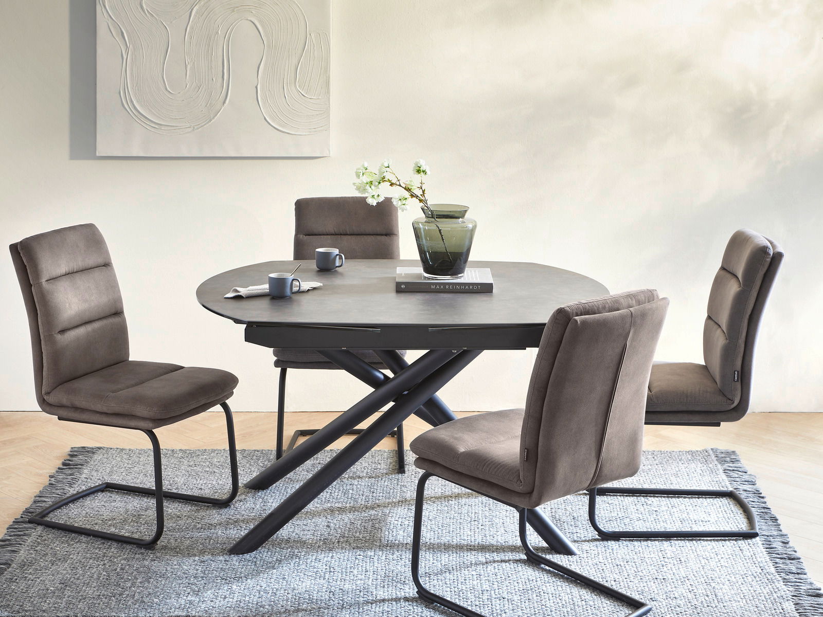 Esszimmer mit vier braunen Freischwinger-Stühlen um einen runden Tisch mit schwarzem Gestell, seitliche Perspektive