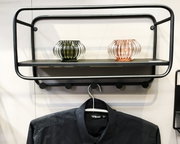Schwarze Wandgarderobe aus Metall mit Ablage und fünf Haken, frontal aus leichter Untersicht fotografiert; darüber stehen zwei gerippte Glas-Teelichthalter, darunter hängt eine schwarze Jacke am Kleiderbügel.