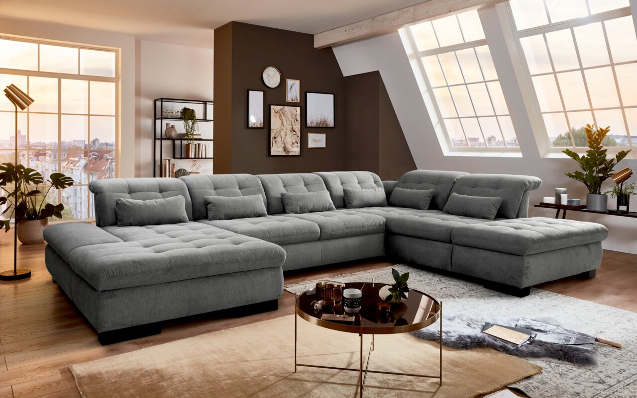 Großes, graues Ecksofa in U-Form in einem modernen Wohnzimmer mit großen Fenstern und stilvoller Dekoration, seitliche Perspektive.
