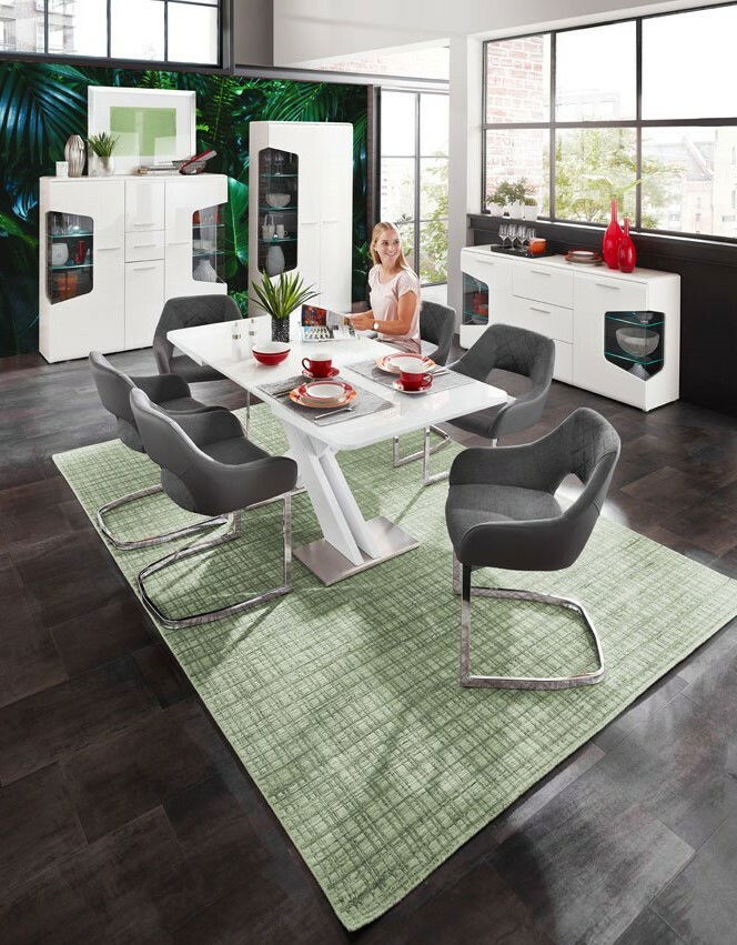 Moderne weiße Vitrine mit zwei Türen, im Hintergrund eines stilvollen Esszimmers mit großen Fenstern und grüner Wanddekoration, aus der Perspektive des Essbereichs betrachtet.