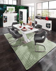 Moderne weiße Vitrine mit zwei Türen, im Hintergrund eines stilvollen Esszimmers mit großen Fenstern und grüner Wanddekoration, aus der Perspektive des Essbereichs betrachtet.