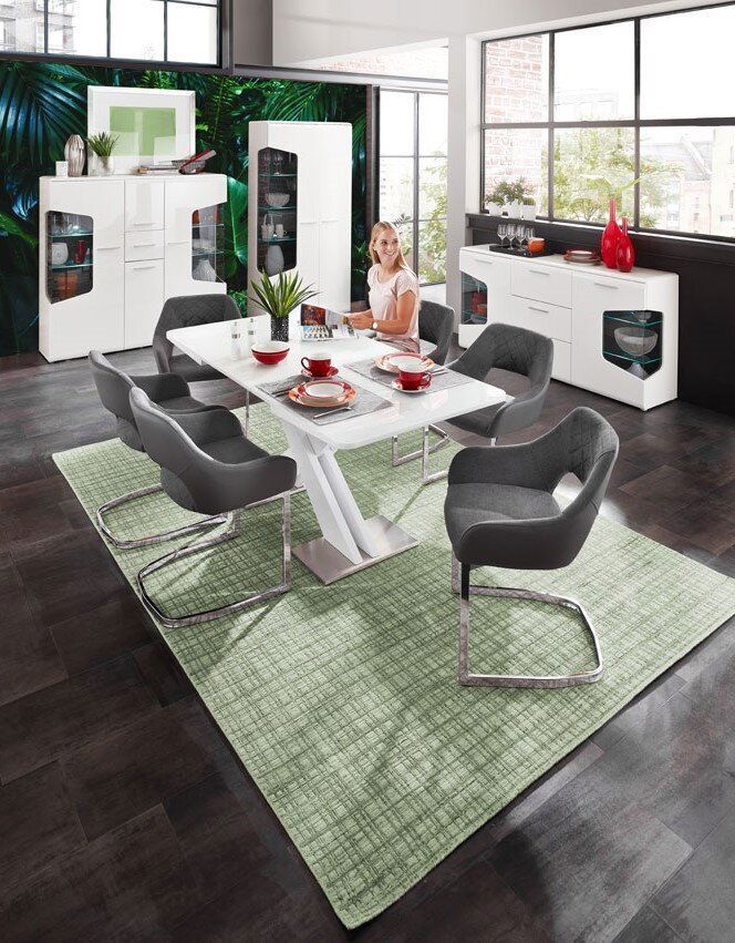 Moderne weiße Vitrine mit zwei Türen, im Hintergrund eines stilvollen Esszimmers mit großen Fenstern und grüner Wanddekoration, aus der Perspektive des Essbereichs betrachtet.