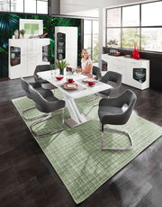 Moderne weiße Vitrine mit zwei Türen, im Hintergrund eines stilvollen Esszimmers mit großen Fenstern und grüner Wanddekoration, aus der Perspektive des Essbereichs betrachtet.