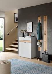 Moderner Flur mit weißem Schuhschrank mit Holz-Akzent, zwei Wandgarderoben aus Holz mit Jacke, Mütze und Schlüsseln sowie Tasche und Schuhen auf dem Boden, fotografiert in frontaler Perspektive leicht von links.