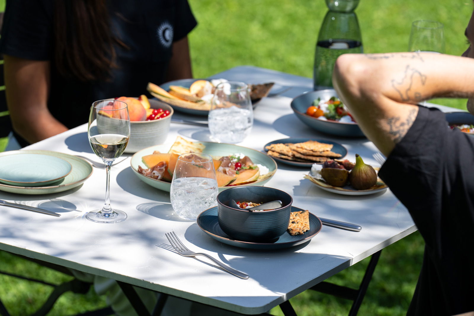 Müslischale 15 cm auf einem gedeckten Tisch im Freien, gefüllt mit Müsli und Obst, umgeben von weiteren Tellern und Gläsern, seitliche Perspektive.