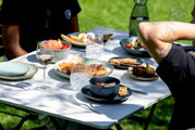 Een mueslischaal van 15 cm op een gedekte tafel in de open lucht, gevuld met muesli en fruit, omringd door andere borden en glazen, zijaanzicht.