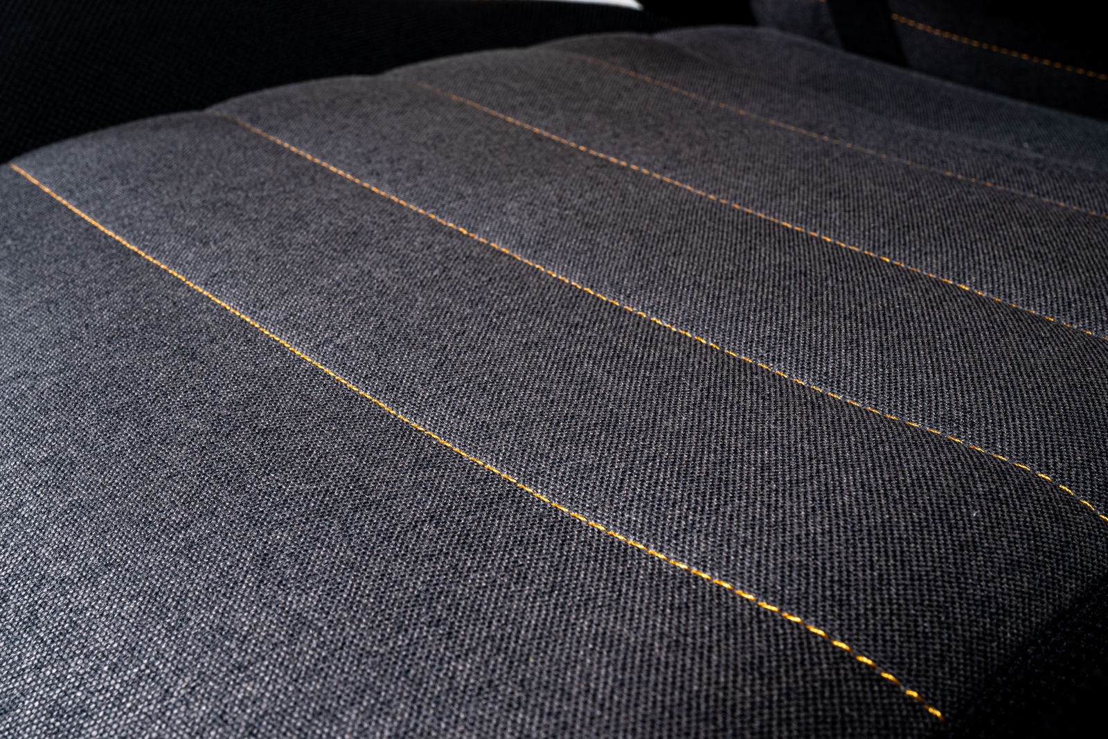 Nahaufnahme der Sitzfläche eines Gaming Stuhls mit grauem Stoff und gelben Nähten, von oben betrachtet.