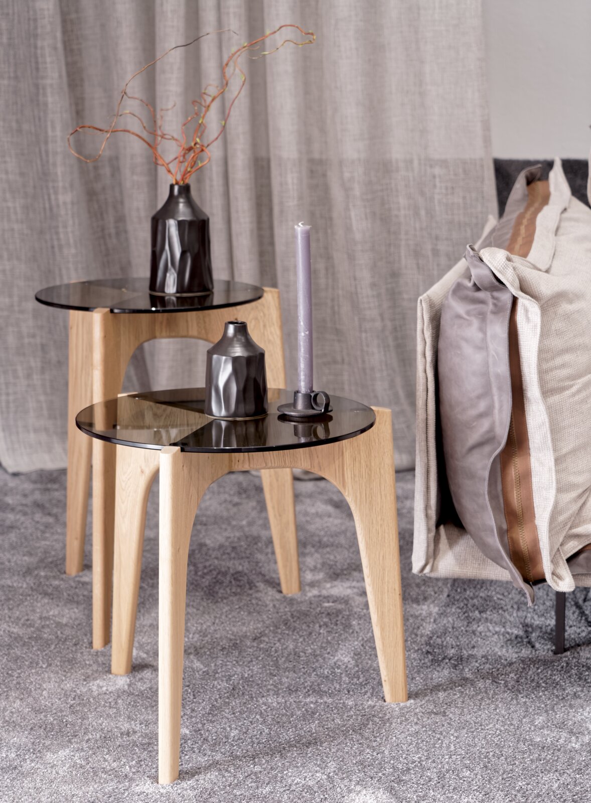 Zwei moderne Beistelltische aus Holz mit schwarzer Glasplatte, dekoriert mit einer Vase und einer Kerze, seitliche Perspektive.