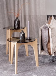 Zwei moderne Beistelltische aus Holz mit schwarzer Glasplatte, dekoriert mit einer Vase und einer Kerze, seitliche Perspektive.