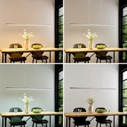 Een slanke, strakke LED-hanglamp boven een houten tafel met stoelen, een vaas en een schaal; vooraanzicht van de lamp in de eethoek.