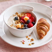 Weiße Schale der Serie NewWave mit Joghurt, frischen Beeren und Müsli, daneben ein Croissant auf einem Teller, aus der Vogelperspektive fotografiert.