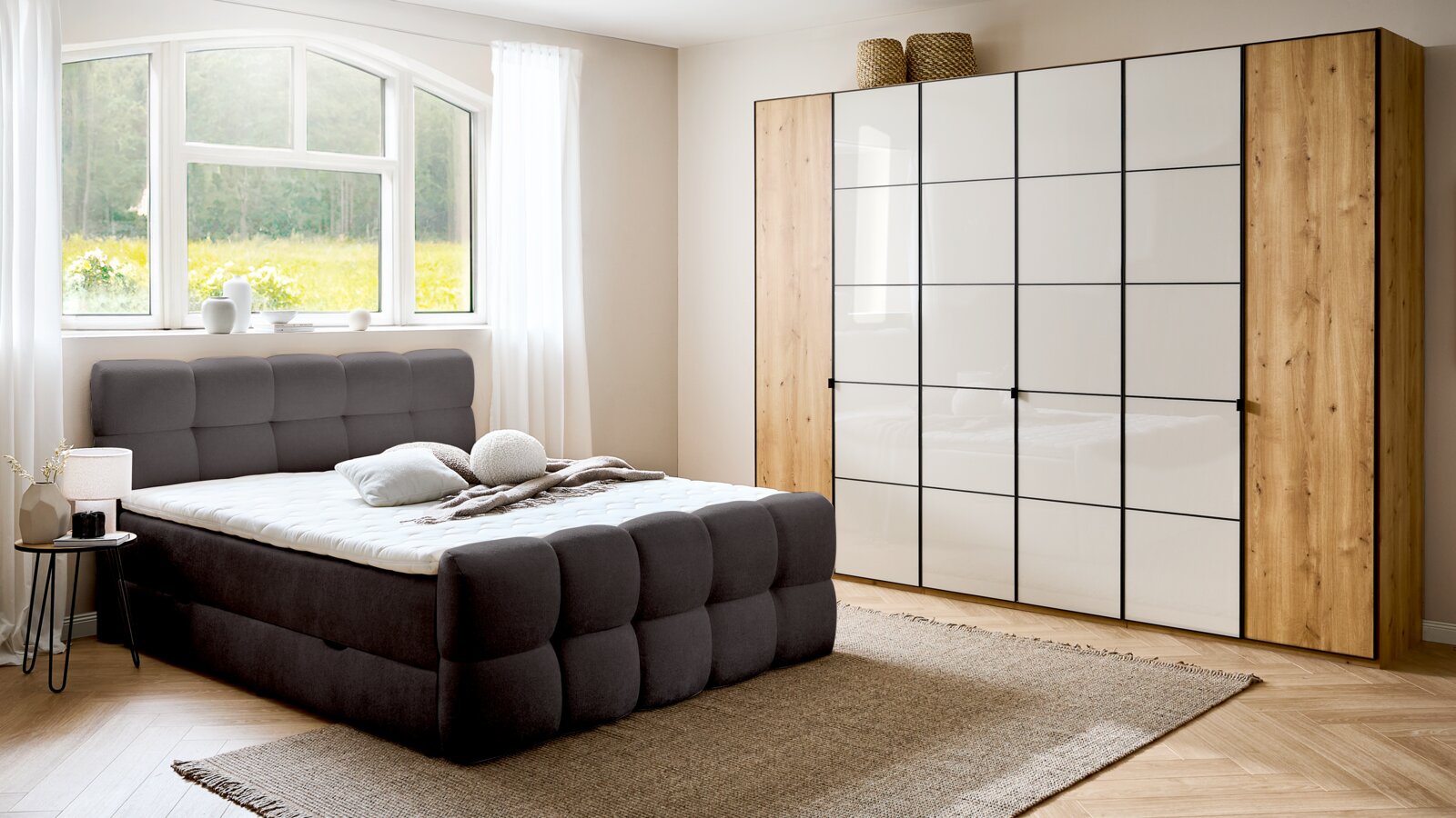 Modernes Boxbett in einem hellen Schlafzimmer mit großem Fenster, grauem gepolstertem Kopfteil und passendem Schrank, seitliche Perspektive.