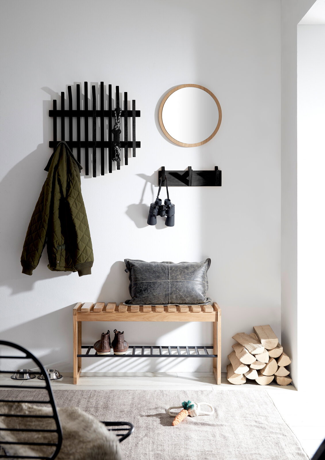 Garderobenbank aus Holz mit schwarzem Metallregal, dekoriert mit Kissen, in einem modernen Flur mit Spiegel und Hakenleiste, seitliche Perspektive