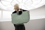Rückansicht einer Person, die eine große, grüne Tasche mit runden Griffen trägt, in einem hellen, modernen Raum.