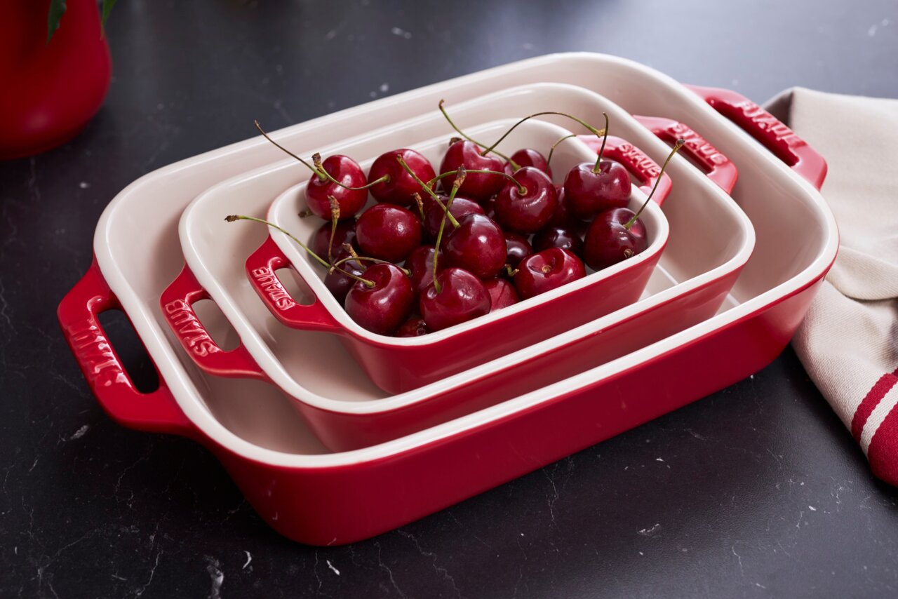 Driedelige ovenschaalset in rood, gestapeld en gevuld met kersen, gefotografeerd vanuit vogelperspectief.