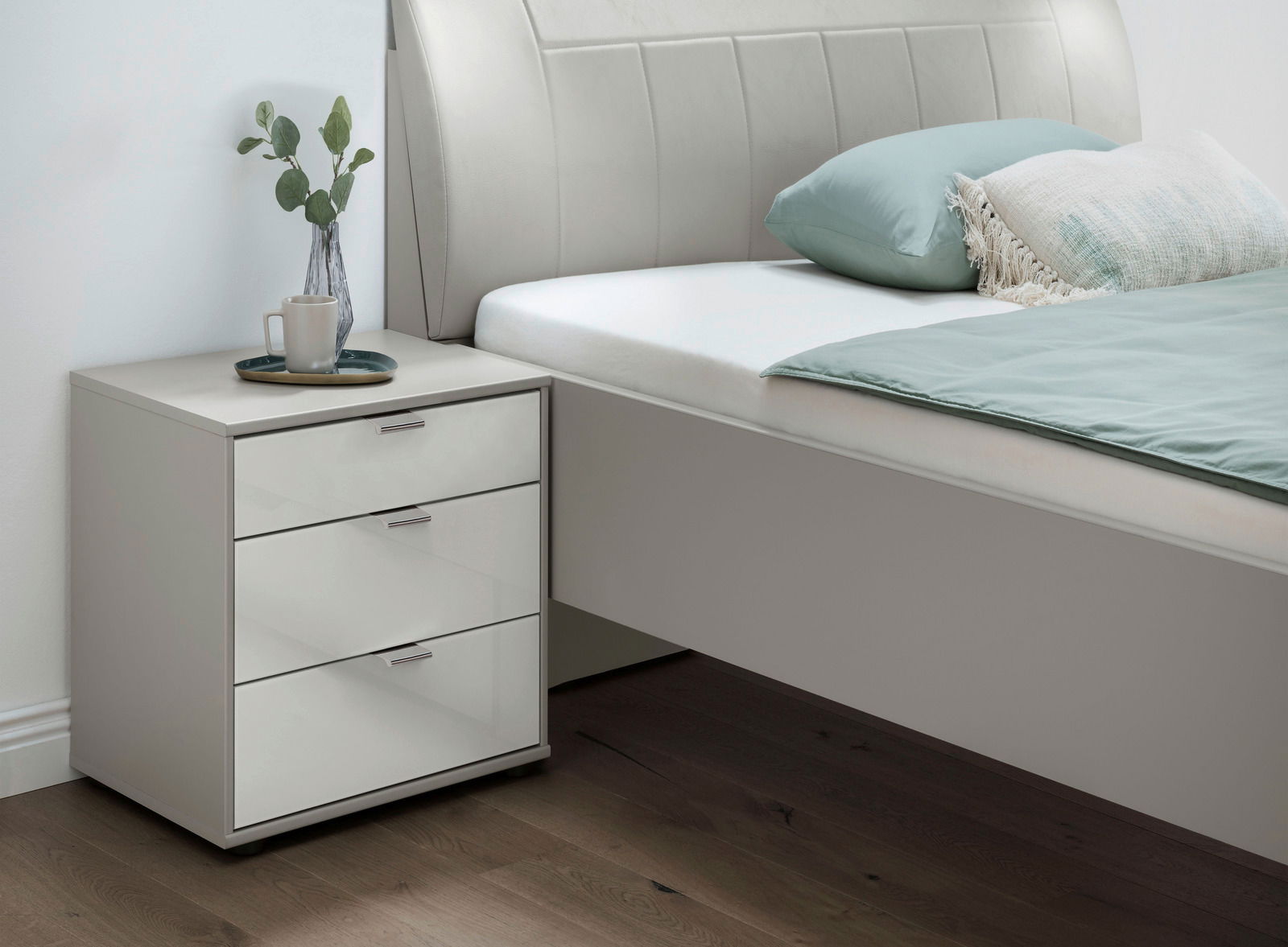 Moderne Nachtkonsole mit drei Schubladen, dekoriert mit einer Vase und Tasse, seitliche Perspektive.