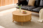 Runder Couchtisch aus Holz mit geriffeltem Design, dekoriert mit einer Vase und einem Teller mit Obst, in einem modernen Wohnzimmer aus der Seitenperspektive.