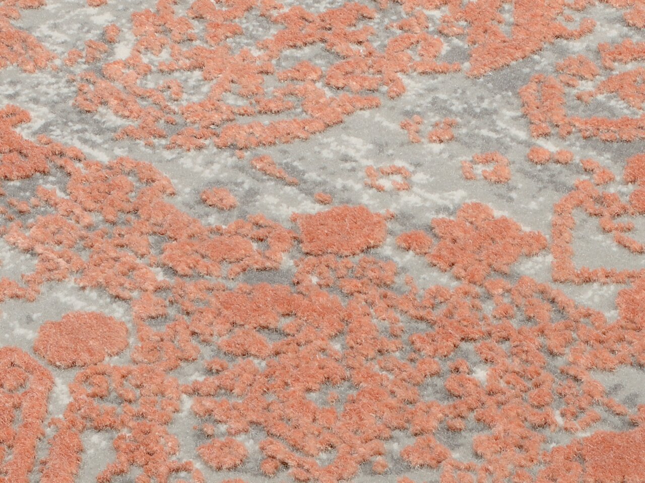 Nahaufnahme eines Designer-Teppichs mit abstraktem Muster in Orange und Grau, von oben betrachtet.