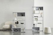 Zwei moderne, weiße Raumteiler mit dekorativen Objekten, von vorne betrachtet. Der linke Raumteiler ist niedriger und breiter, der rechte ist höher und schmaler. Beide stehen auf einem hellen Boden vor einer weißen Wand.