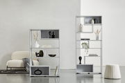 Zwei moderne, weiße Raumteiler mit dekorativen Objekten, von vorne betrachtet. Der linke Raumteiler ist niedriger und breiter, der rechte ist höher und schmaler. Beide stehen auf einem hellen Boden vor einer weißen Wand.