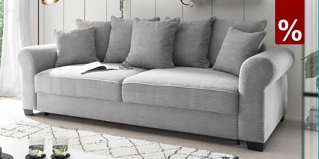 Modernes graues 3-Sitzer-Sofa mit Cordbezug und Kissen vor weißer Wandpaneel-Optik im skandinavischen Wohnzimmer.