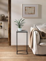 Moderner Beistelltisch SILKE mit schwarzem Metallgestell und grauer Tischplatte, seitliche Perspektive, dekoriert mit einer Pflanze.