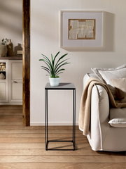 Moderner Beistelltisch SILKE mit schwarzem Metallgestell und grauer Tischplatte, seitliche Perspektive, dekoriert mit einer Pflanze.