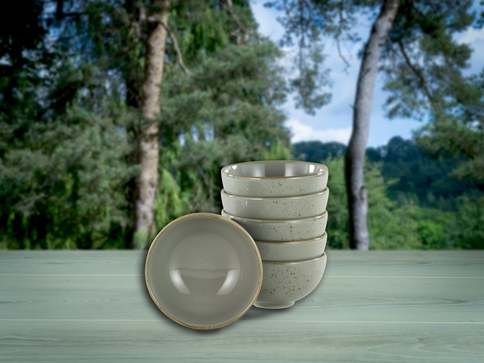 Creatable Dipschale 6-tlg NATURE COLLECTION Stapel aus fünf gesprenkelten Keramikschalen in Beige auf einem hellen Holztisch vor unscharfem Waldhintergrund, eine Schale vorne liegend; Perspektive: leicht von vorne mit leicht erhöhter Ansicht.