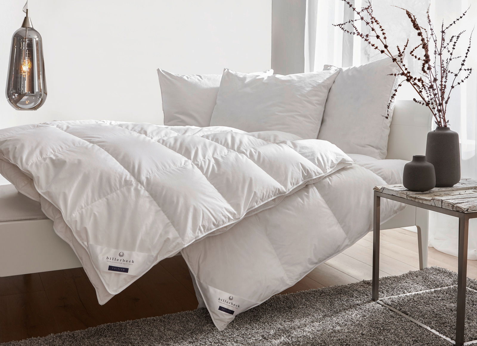 billerbeck Daunendecke POLARSTERN Daunendecke und Kopfkissen auf einem Sofa, seitliche Perspektive, mit dekorativen Vasen auf einem Tisch im Vordergrund.