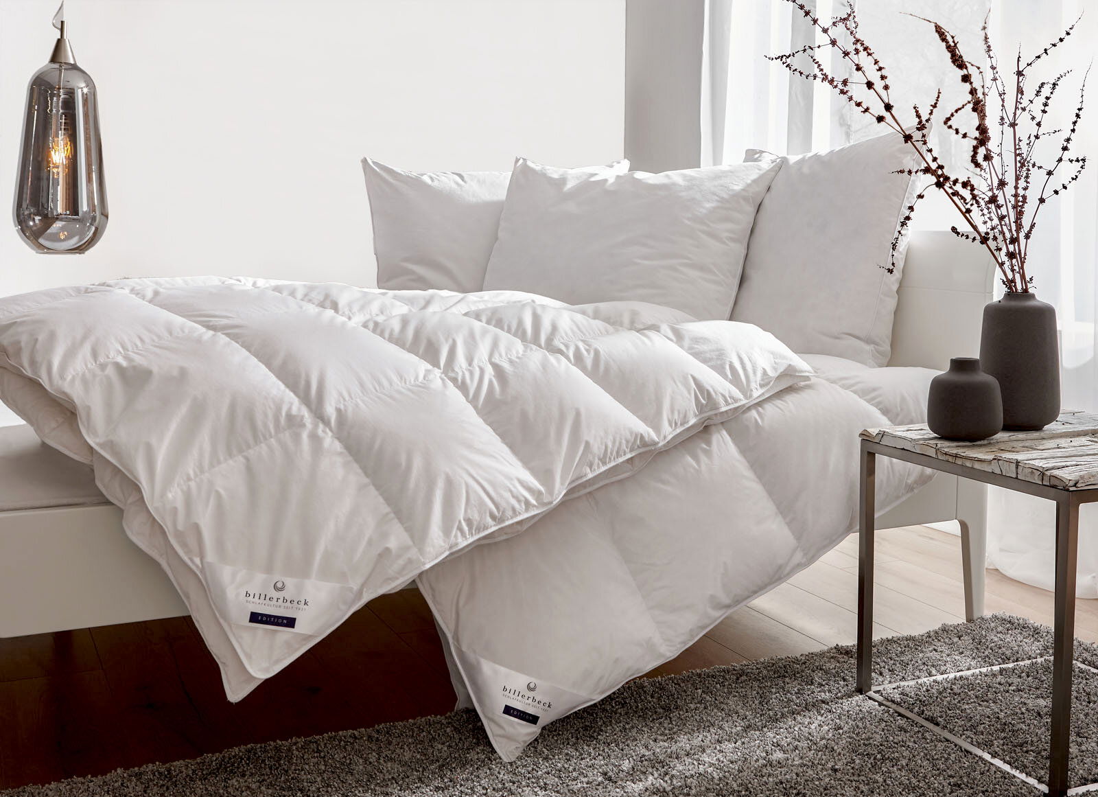 Daunendecke und Kopfkissen auf einem Sofa, seitliche Perspektive, mit dekorativen Vasen auf einem Tisch im Vordergrund.