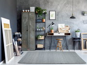 Moderner Raum mit grauem Handweb Teppich im Vordergrund, umgeben von industriellen Möbeln und Pflanzen.