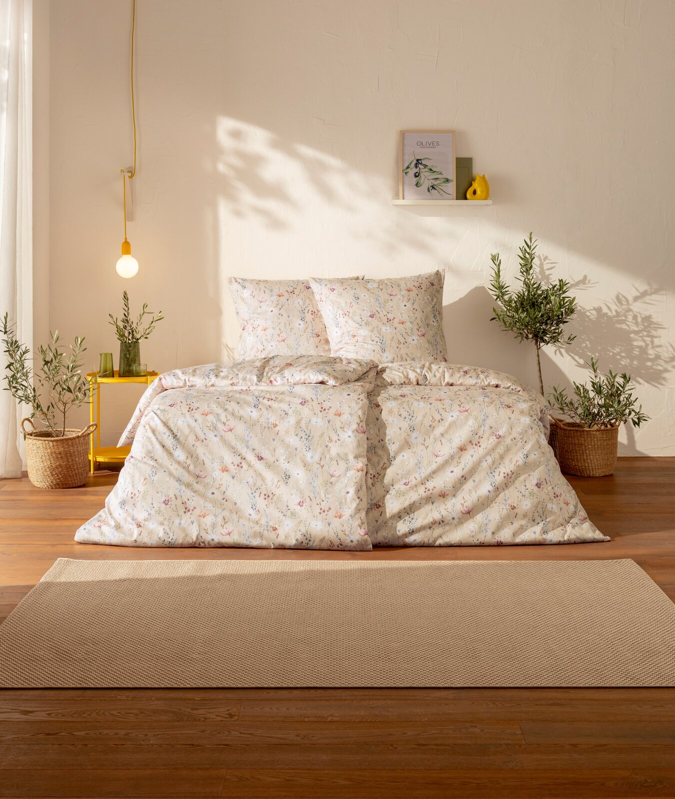 Estella Mako-Satin Bettwäsche 135/200cm CELESTE Frontalansicht eines gemütlich gestylten Bettes mit cremefarbener Bettwäsche im zarten Blumenmuster, zwei passenden Kissen und dekorativen Pflanzen im hellen Schlafzimmer bei warmem Tageslicht.