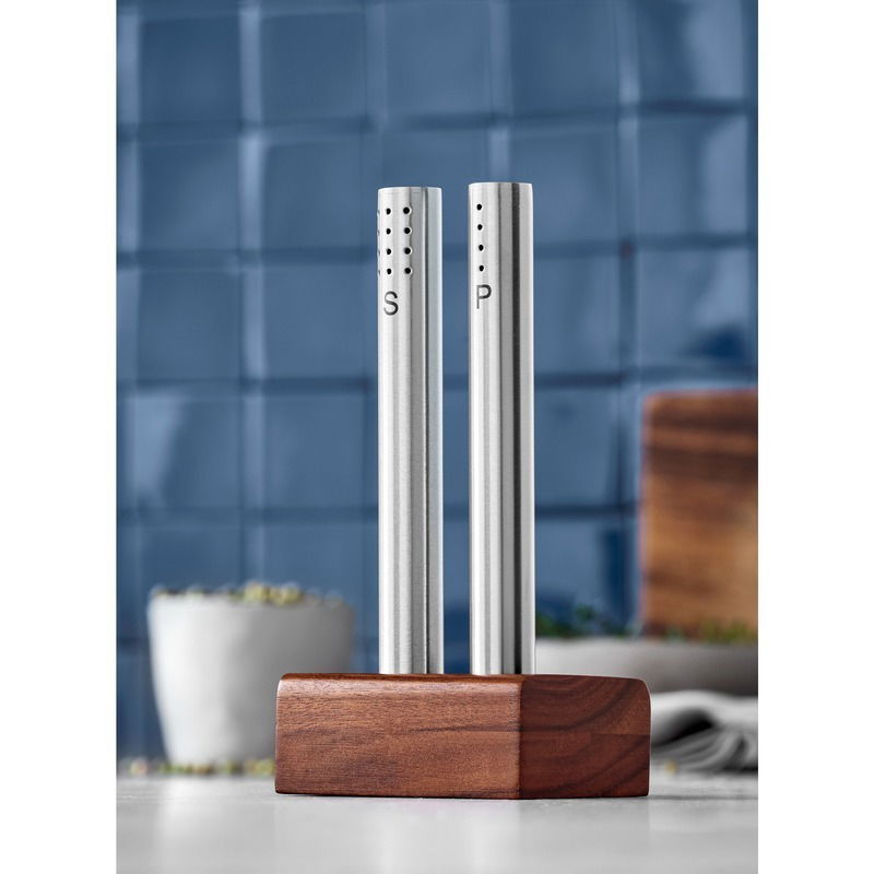 Modernes Salz- und Pfeffer-Set aus Edelstahl mit Holzständer, frontal abgebildet vor einer blauen Kachelwand.
