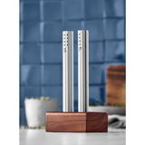 Modernes Salz- und Pfeffer-Set aus Edelstahl mit Holzständer, frontal abgebildet vor einer blauen Kachelwand.