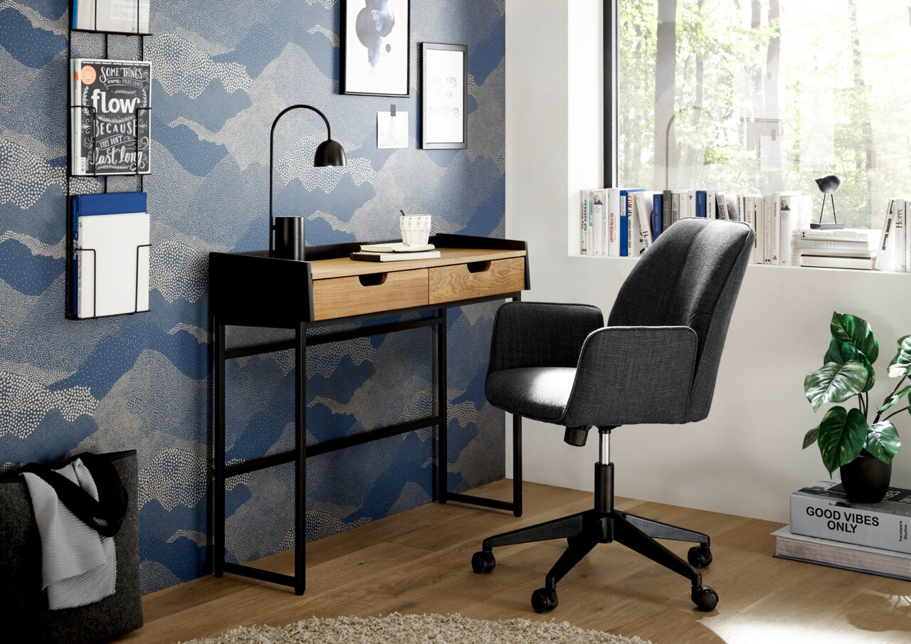 Moderner Schreibtisch mit zwei Schubladen aus Holz und schwarzem Metallgestell, seitliche Perspektive, mit grauem Bürostuhl und dekorativer Wand im Hintergrund.