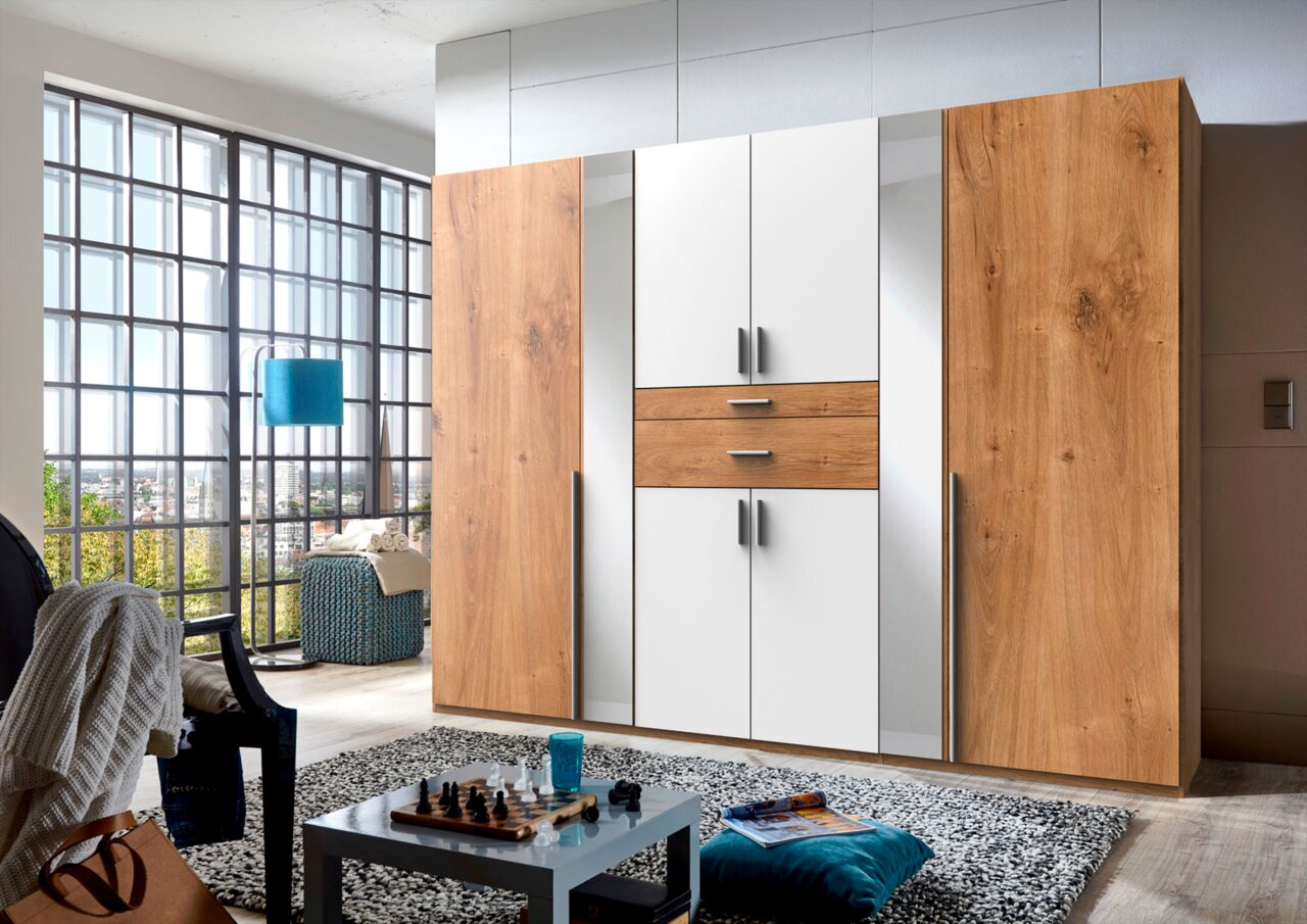 Z2 Drehtürenschrank 8-türig ODESSA Moderner 8-türiger Drehtürenschrank in Holzoptik und Weiß, frontal abgebildet in einem stilvollen Wohnzimmer mit großen Fenstern.