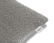 Graue Zierkissenhülle mit strukturierter Oberfläche, perspektivisch von der Seite fotografiert, mit sichtbarem Etikett der Schöner Wohnen Kollektion.