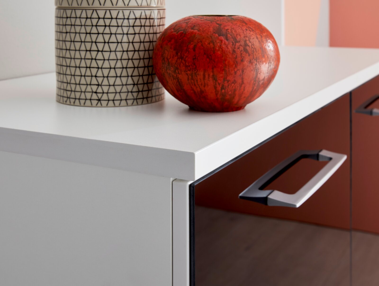 Nahaufnahme eines modernen Sideboards mit weißer Oberfläche und roten Schubladen, dekoriert mit einer roten Vase und einem gemusterten Behälter.