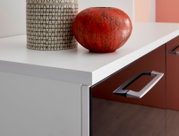 Nahaufnahme eines modernen Sideboards mit weißer Oberfläche und roten Schubladen, dekoriert mit einer roten Vase und einem gemusterten Behälter.