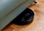 Ein Saugroboter, der unter einem Sofa auf einem Holzboden reinigt, aus seitlicher Perspektive.