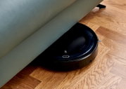 Ein Saugroboter, der unter einem Sofa auf einem Holzboden reinigt, aus seitlicher Perspektive.