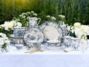Blau-weißes Porzellan-Geschirrset mit floralem Muster (Teller, Schalen, Tassen und Becher) dekorativ auf weißer Tischdecke im Garten arrangiert, fotografiert in frontaler Perspektive auf Augenhöhe.